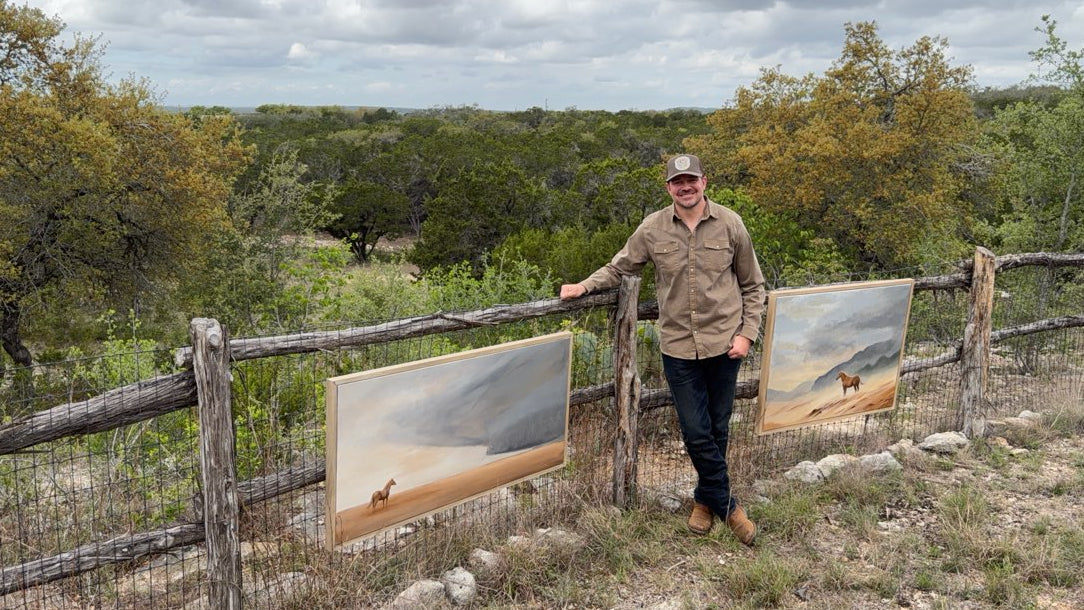 Shane Moody standing on his property with two of his landscape paintings, surrounded by nature on his Texas ranch.